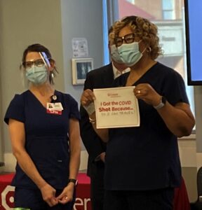 COVID VACCINATION Cooper Rosetta Oliver, RN first recipient holding sign