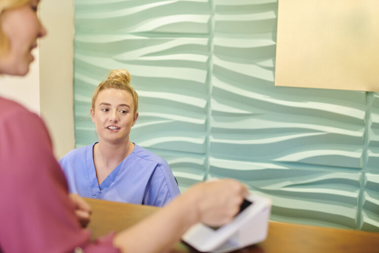 patient at a doctor's office taps their credit card as the receptionist looks on