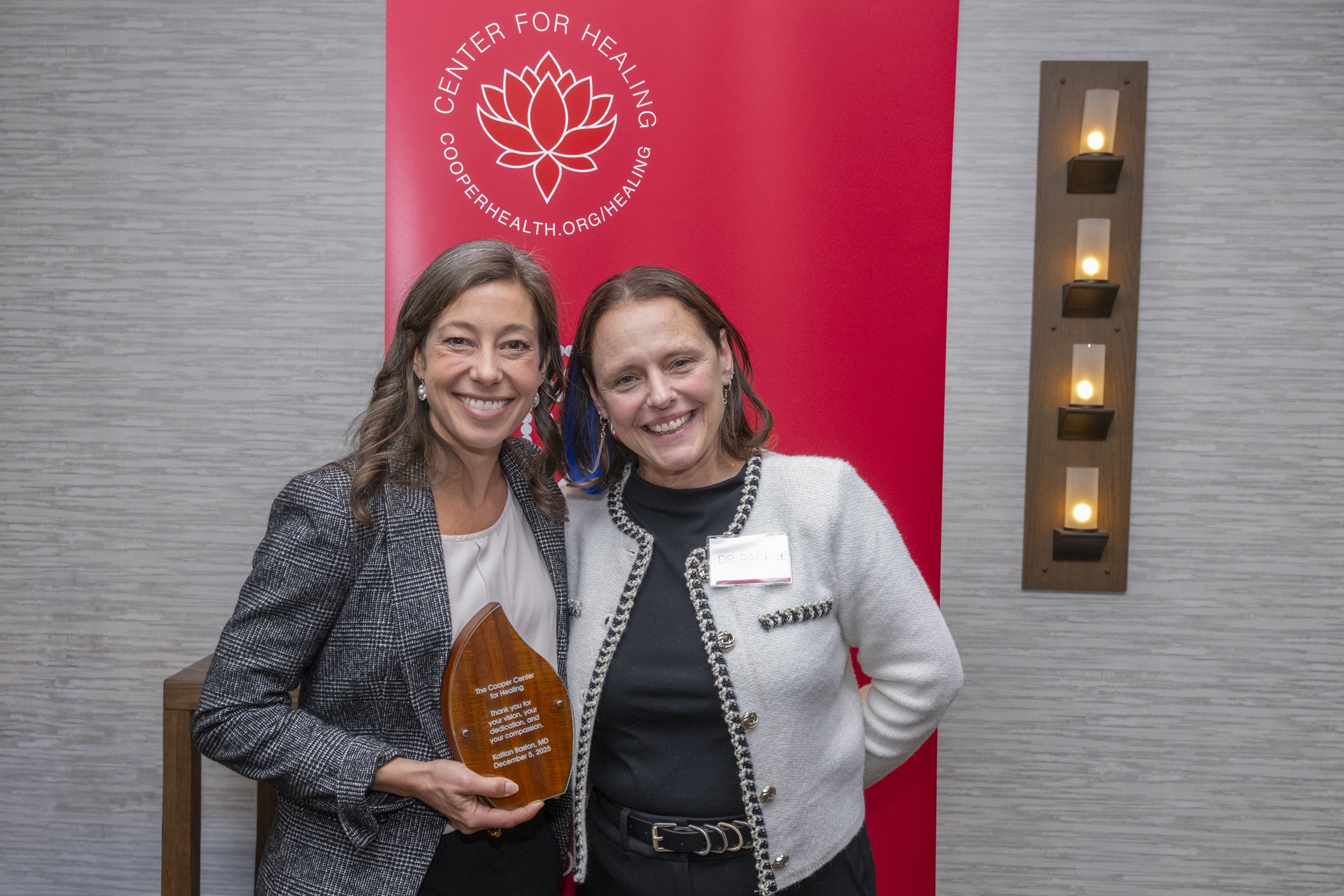 Two women smiling in front of a red Center for Healing banner. Woman on the left is holding an award plaque.